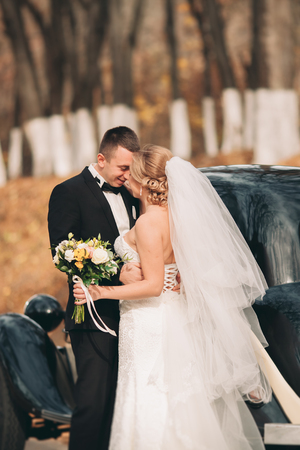 Stylish wedding couple, bride and groom hugging near retro car in autumn.の写真素材