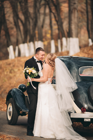 Stylish wedding couple, bride and groom hugging near retro car in autumn.の写真素材