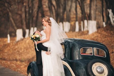Stylish wedding couple, bride and groom hugging near retro car in autumn.の写真素材
