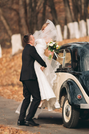 Stylish wedding couple, bride and groom hugging near retro car in autumn.の写真素材