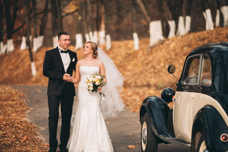 Stylish wedding couple, bride and groom near retro car in autumn.の写真素材