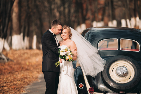 Stylish wedding couple, bride and groom hugging near retro car in autumn.の写真素材