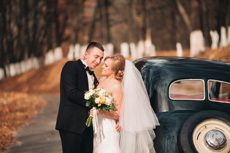 Stylish wedding couple, bride and groom hugging near retro car in autumn.の写真素材