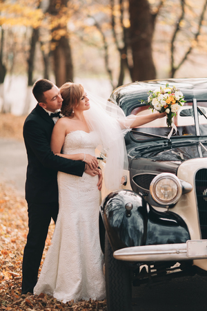 Stylish wedding couple, bride and groom hugging near retro car in autumn.の写真素材
