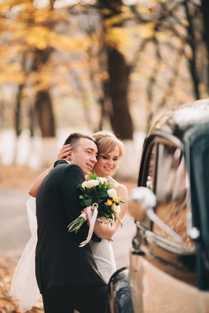 Stylish wedding couple, bride and groom hugging near retro car in autumn.の写真素材