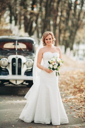 Beautiful happy bride with bouquet near retro car in autumn.の写真素材