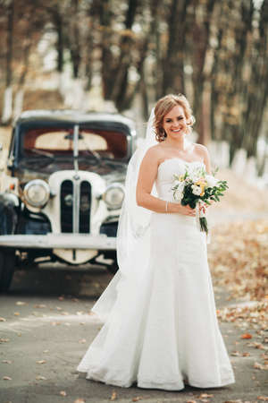 Beautiful happy bride with bouquet near retro car in autumn.の写真素材