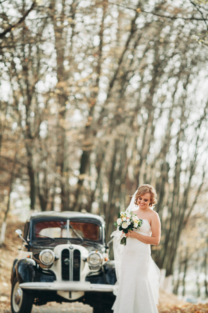 Beautiful happy bride with bouquet near retro car in autumn.の写真素材