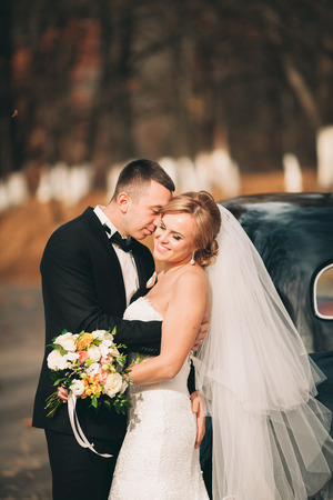 Stylish wedding couple, bride and groom hugging near retro car in autumn.の写真素材