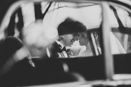 Stylish wedding couple, bride and groom kissing and hugging near retro car in autumn.の写真素材