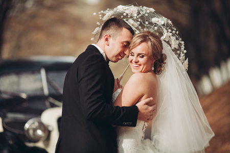 Stylish wedding couple, bride and groom hugging near retro car in autumn.の写真素材