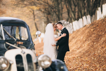 Stylish wedding couple, bride and groom hugging near retro car in autumn.の写真素材