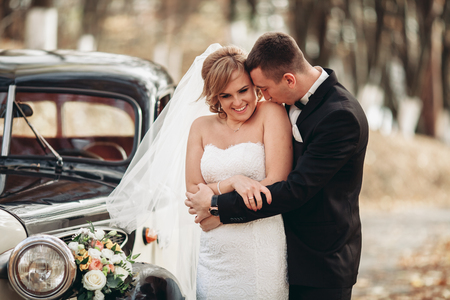 Stylish wedding couple, bride and groom hugging near retro car in autumn.の写真素材