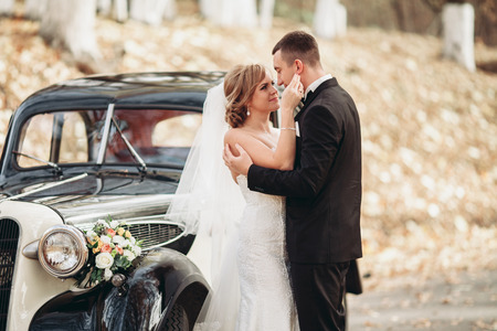 Stylish wedding couple, bride and groom hugging near retro car in autumn.の写真素材