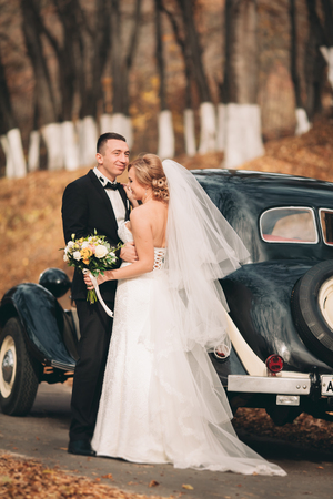 Stylish wedding couple, bride and groom hugging near retro car in autumn.の写真素材