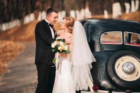 Stylish wedding couple, bride and groom hugging near retro car in autumn.の写真素材