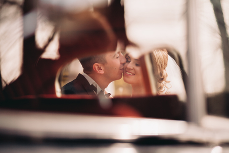 Stylish wedding couple, bride and groom kissing and hugging near retro car in autumn.の写真素材
