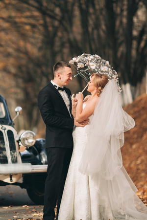 Stylish wedding couple, bride and groom hugging near retro car in autumn.の写真素材
