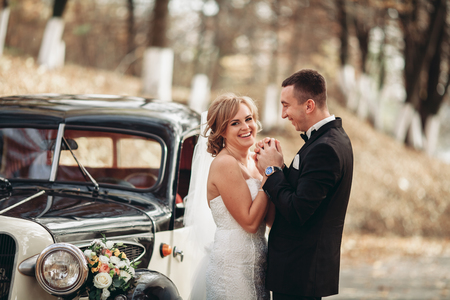 Stylish wedding couple, bride and groom hugging near retro car in autumn.の写真素材