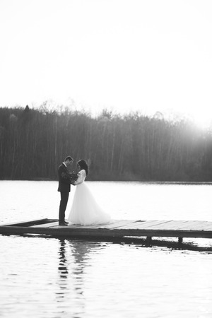 Elegant beautiful wedding couple posing near a lake at sunset.の写真素材