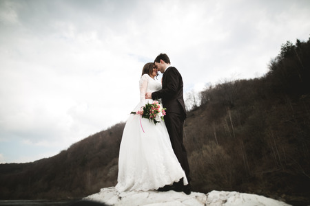 Beautifull wedding couple kissing and embracing near river with stones.の写真素材
