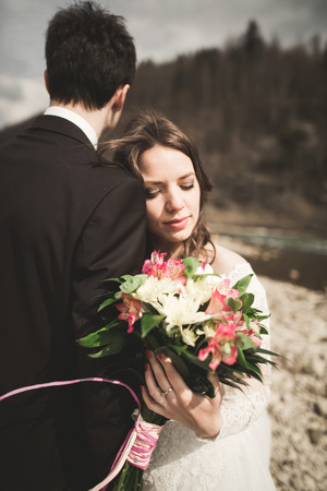 Happy wedding couple, bride and groom posing neat river against backdrop of the mountains.の写真素材