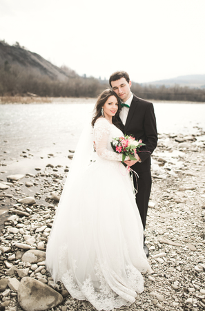 Happy wedding couple, bride and groom posing neat river against backdrop of the mountains.の写真素材