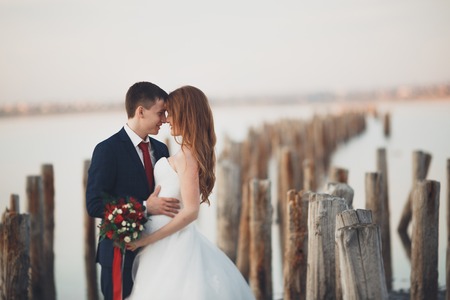 Wedding couple, groom, bride with bouquet posing near sea on sunset.の写真素材