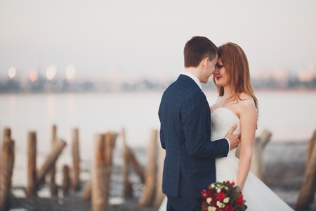 Wedding couple, groom, bride with bouquet posing near sea on sunset.の写真素材