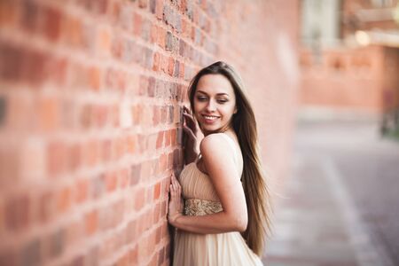 Beautiful girl with long hair long dress perfect shape tanned body posing near wall.の写真素材