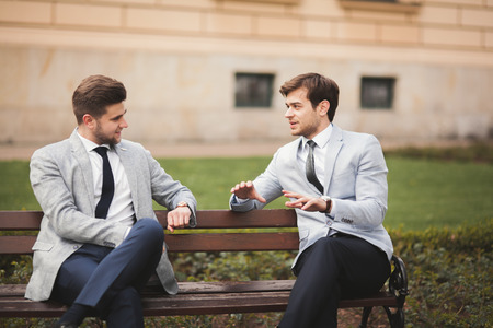 Two stylish businessmen speaking and smiling outdoors.の写真素材
