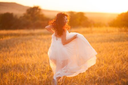 Happy beautiful young bride outside on a summer meadow at the sunset.の写真素材