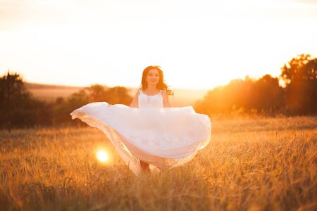 Happy beautiful young bride outside on a summer meadow at the sunset.の写真素材