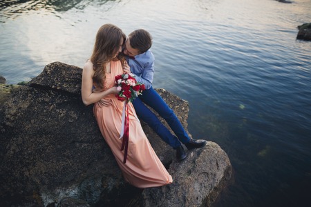 Wedding couple kissing and hugging on rocks near blue sea.の写真素材