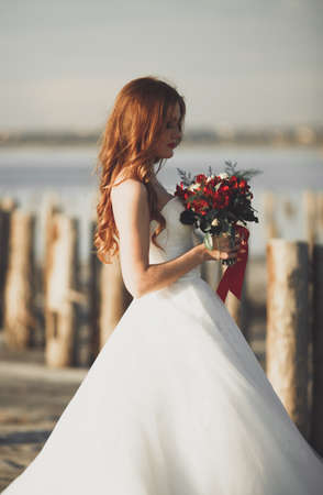 Pretty lady, bride posing in a wedding dress near sea on sunset.の写真素材