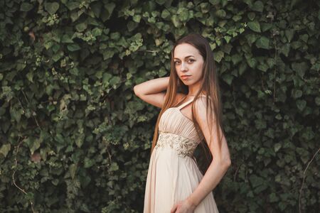 Beautiful girl, model near the wall of leaves and bushes in park.の写真素材