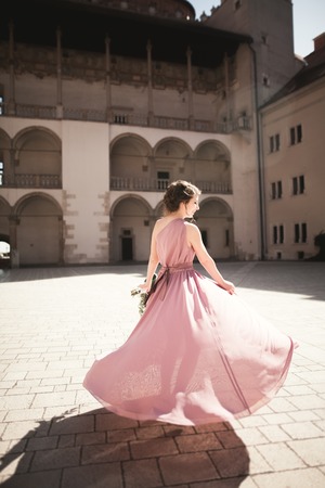 Portrait of a beautiful young bride that stands between the columns near old building and holding bridal bouquet.の写真素材