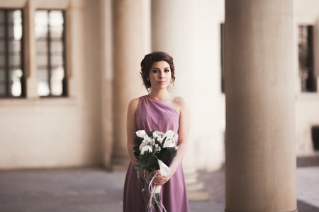 Portrait of a beautiful young bride that stands between the columns near old building and holding bridal bouquet.の写真素材