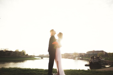 Elegant beautiful wedding couple posing near river at sunset.の写真素材