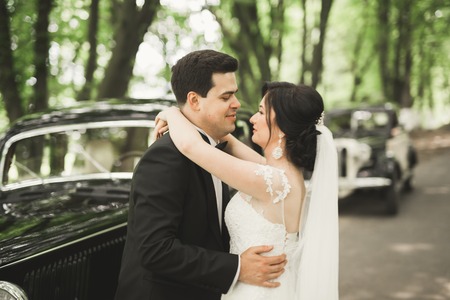 Stylish wedding couple, bride and groom kissing and hugging near retro car in autumn.の写真素材