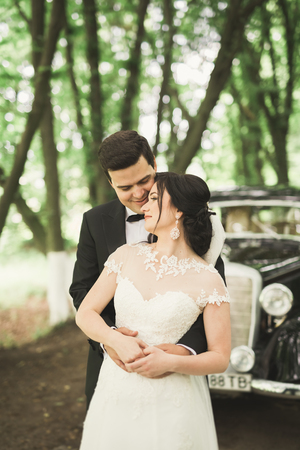 Stylish wedding couple, bride and groom kissing and hugging near retro car in autumn.の写真素材