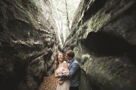 Gorgeous wedding couple kissing and hugging in forest with big rocks.の写真素材