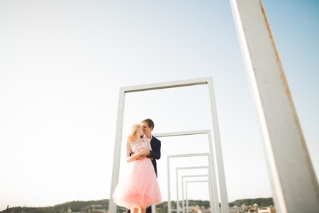 Young couple in love posing on roof with perfect city view holding hands and hugging . Beautiful sunset.の写真素材