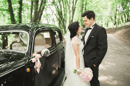 Beautiful newlywed couple posing near retro black car.の写真素材