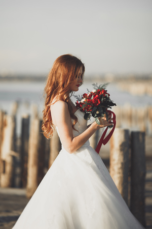 Beautiful young bride with bridal bouquet posing on the background sea.の写真素材