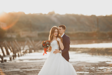 Wedding couple, groom, bride with bouquet posing near sea on sunset.の写真素材