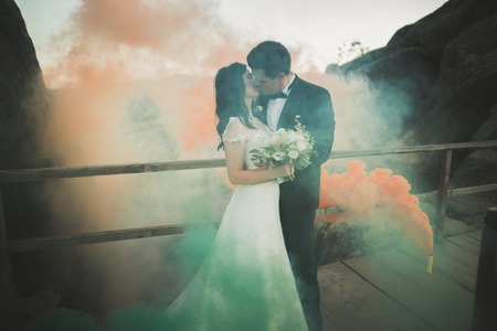 Wedding couple posing near rocks with colored smoke behind them.の写真素材