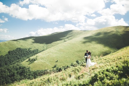 Young newly wed couple, bride and groom kissing, hugging on perfect view of mountains, blue sky.の写真素材