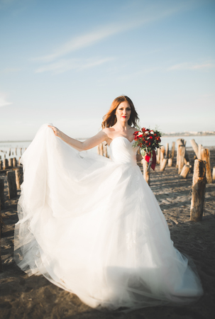 Beautiful young bride with bridal bouquet posing on the background sea.の写真素材
