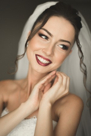 Beautiful young bride with makeup and hairstyle in bedroom, newlywed woman final preparation for wedding. Happy girl waiting groom. Portrait soft focus.の写真素材